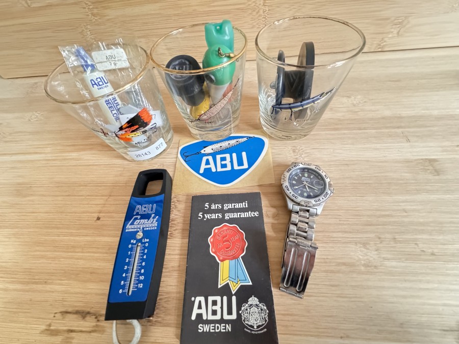 ABU Dekomaterial, 3 Whiskey Gläser mit Köderaufdruck (Toby, ABU Fly, Hilo), alter Aufkleber, Garantiekarte, 2 Exzenter Gewichte original verpackt, Rollenöler, E-spule Metall C 66, Montageschlüssel, gebrauchte ABU Garcia Uhr, 2 verschiedene Turniergewichte, Gewicht mit Magnet für Fliegenweitwurf, Combo-Waage, Gummirutenendstück, Rarität