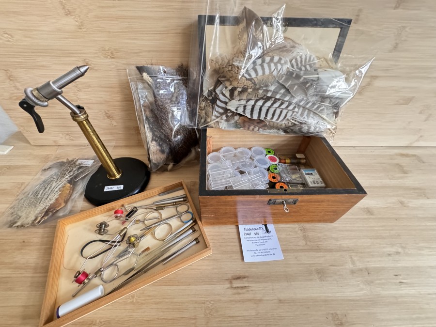 Fliegenbindeausrüstung, HMH Bindestück mit Tischplatte, schöne Holzkiste mit Bindewerkzeug, 2 Scheren, 4 Bobbinhalter, 3 Hechelklemmen, Pinzette, Dubbingnadel, Tungstenkugeln, 15 Boxen mit verschiedenen Tiemco Haken, 2 Monobond KitsRehhaar, Fellreste, Konvolut Federn