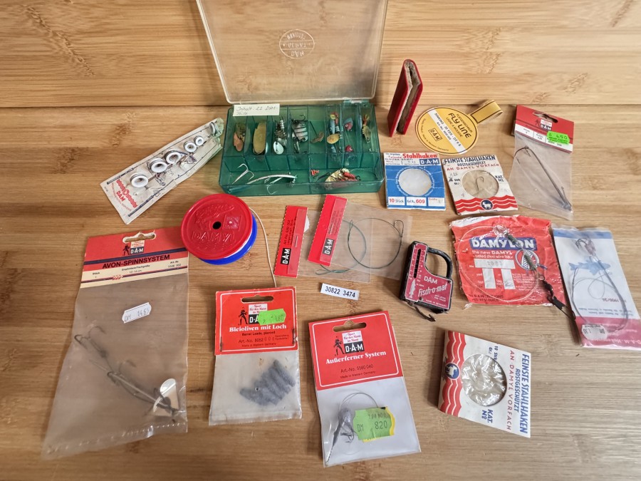 DAM-Konvolut mit vielen Teilen in Originalverpackung, dazu noch eine DAM-Köderschachtel mit 22 DAM-Teilen (z.B. Anstecknadel), kleine DAM-Waage mit Maßband, Fliegenschnur-Reinigungsbüchlein, kompletter Keramikringsatz auf alter Karte